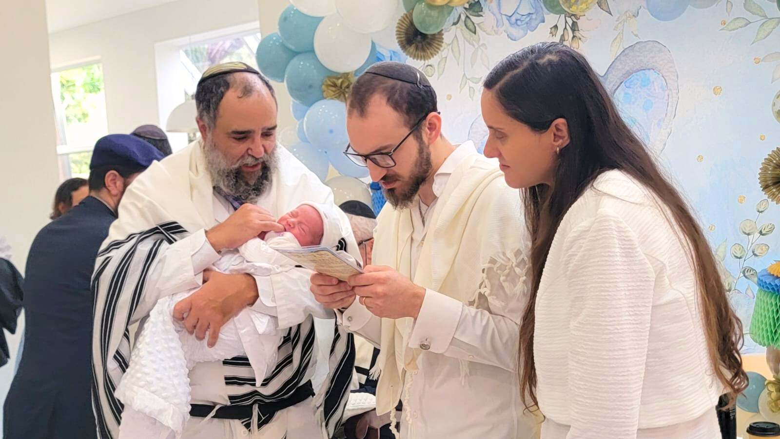 Rabbi Yossi Srugo holds a newborn while the parents read the blessings during a Brit Milah in South Florida