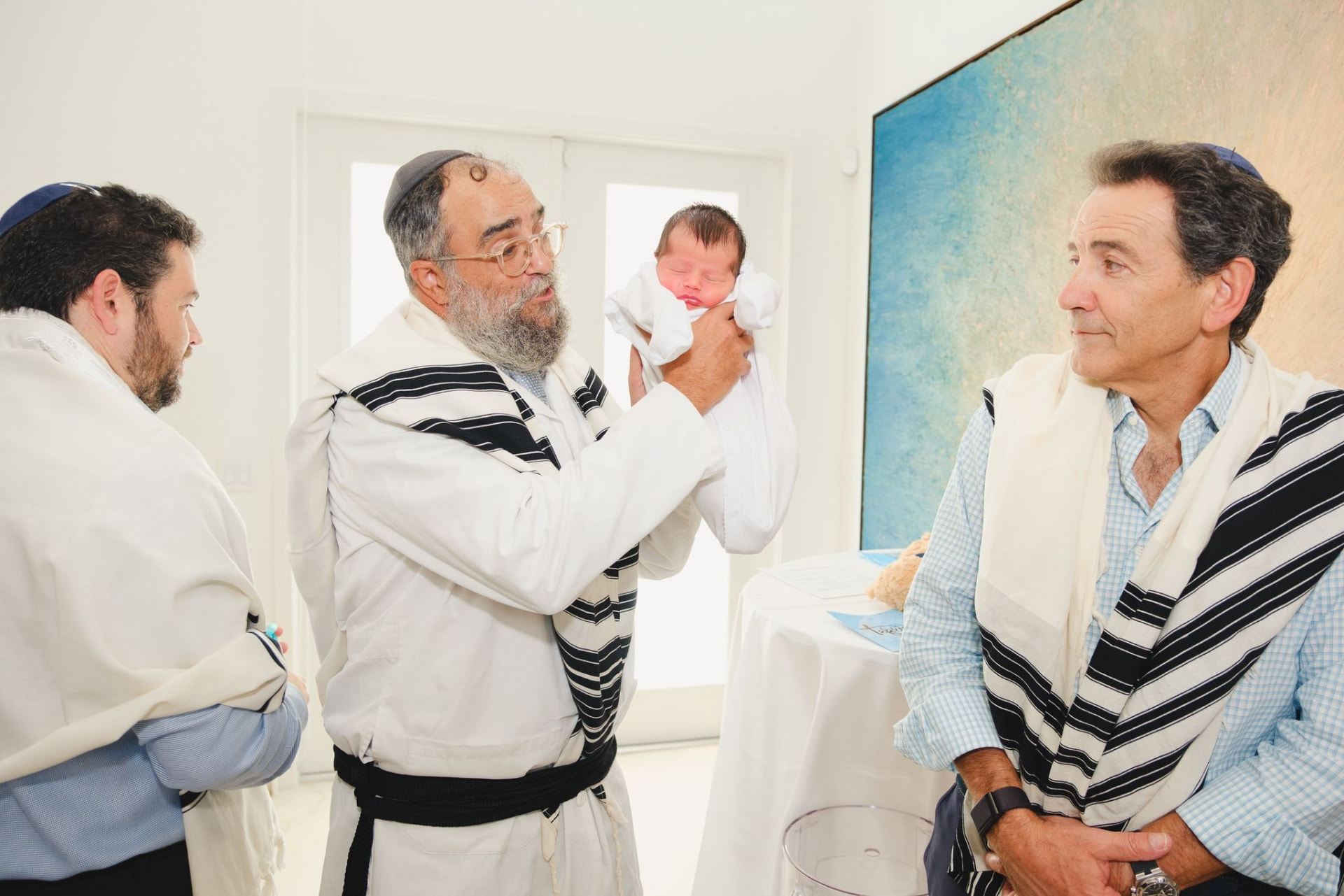 Rabbi Yossi Srugo smiling while holding a newborn wrapped in white before a Brit Milah on Rosh Hashanah in South Florida