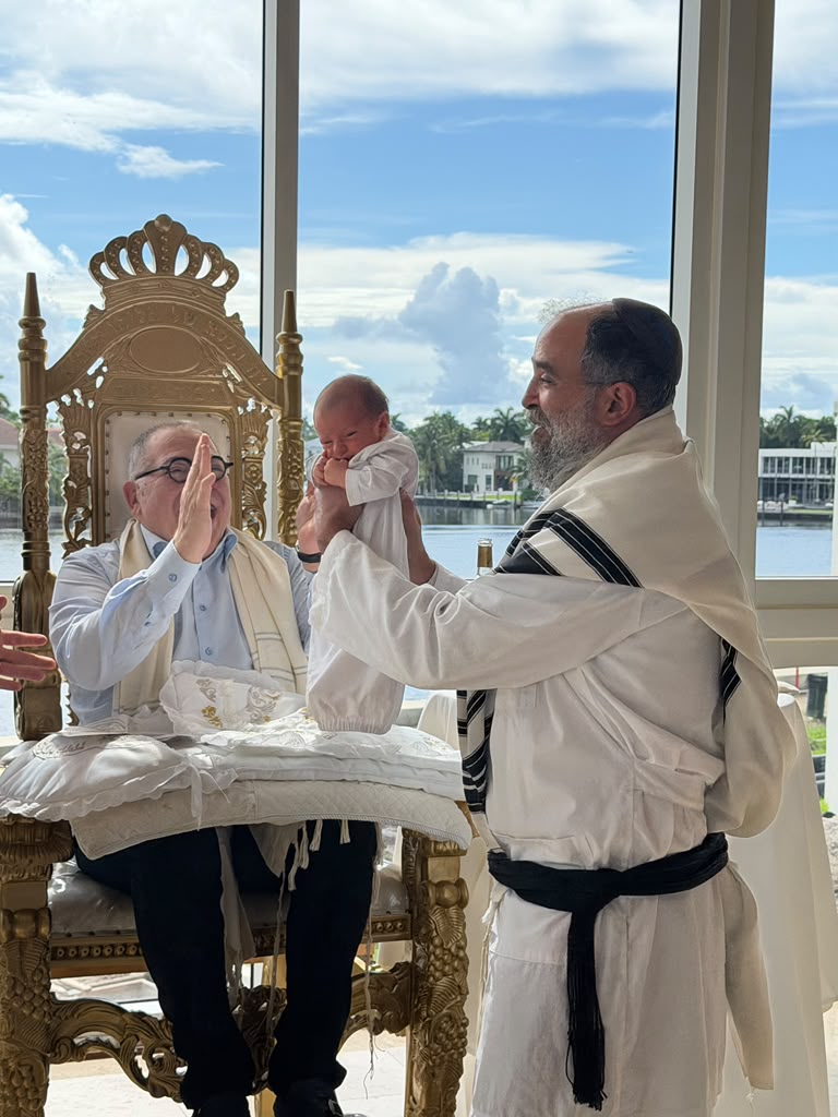 Rabbi Yossi Srugo lifting the baby before the bris ceremony, blessing him in front of the sandek